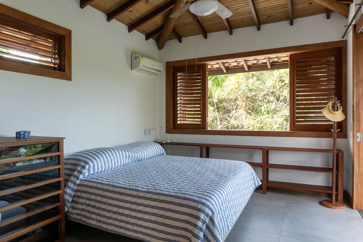 Quarto com cama listrada e janelas de madeira