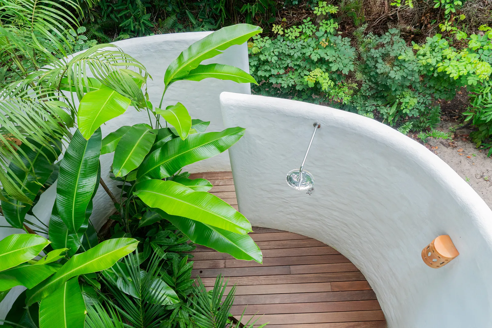 Parede curva branca com chuveiro entre plantas